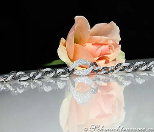 Schwarz-weißes Armband mit Diamanten auf glänzender Oberfläche, Rosenblüte im Hintergrund.