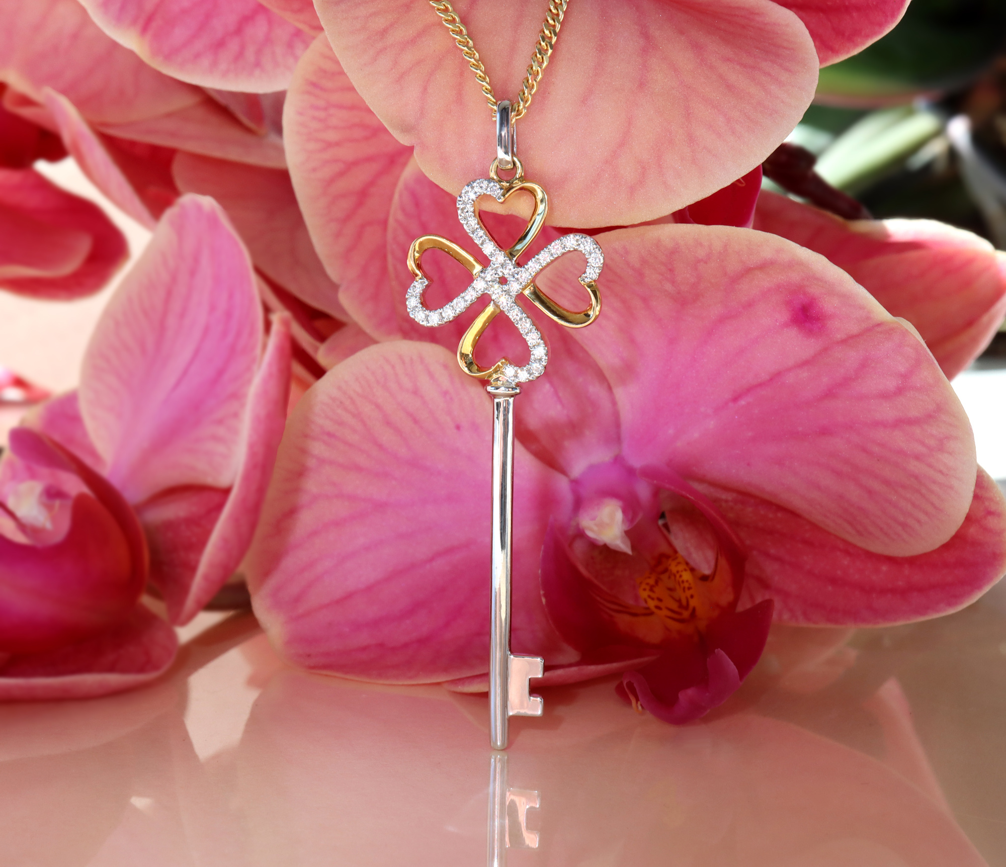 Orchideenblüten-Hintergrund mit Goldschlüsselanhänger mit Brillanten, Detailaufnahme