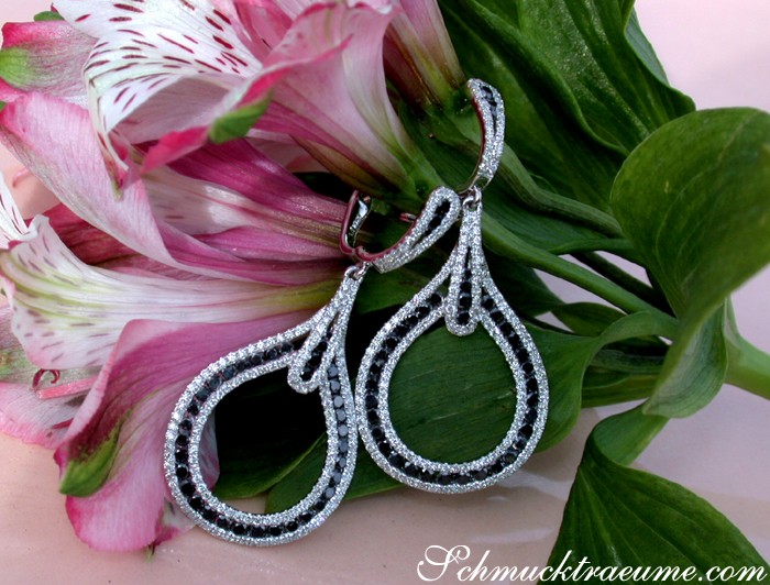 Teardrop-Ohrringe aus Weißgold mit Brillanten und schwarzen Diamanten, Detailaufnahme, auf Blumen abgestellt.