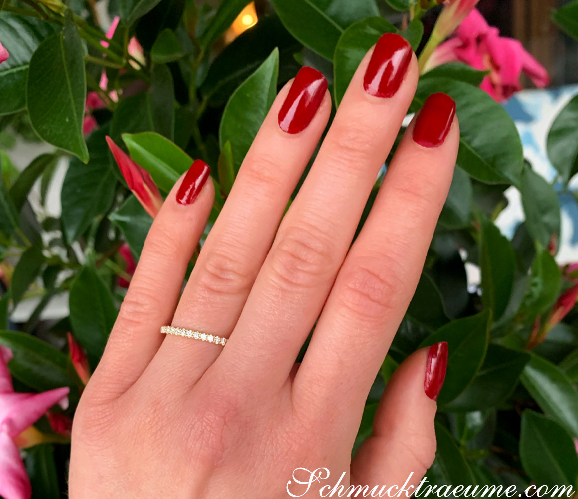 Hand mit roten Nagellack und funkelndem Brillanten Memory Ring vor grünen Blättern