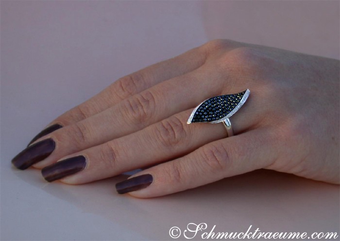 Weißgold-Ring mit schwarzen Diamanten im Blatt-Design auf Hand mit dunklen Nagellack.