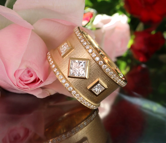 Goldener Ring mit Diamanten und Rosenblüte im Hintergrund Goldener Ring mit Diamanten und Rosenblüte im Hintergrund