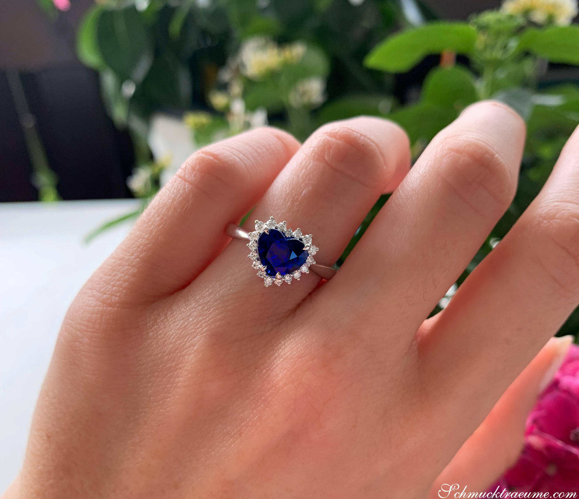Hand mit Herz-Saphir-Ring, umgeben von grünen Pflanzen