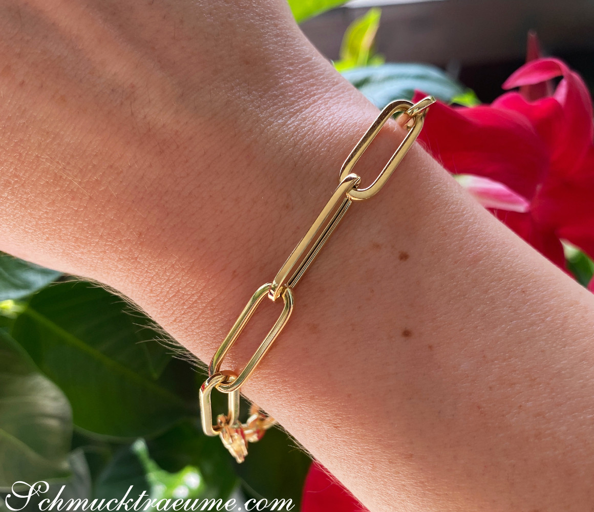 Goldiges Paperclip-Armband auf Hand mit Blumen im Hintergrund