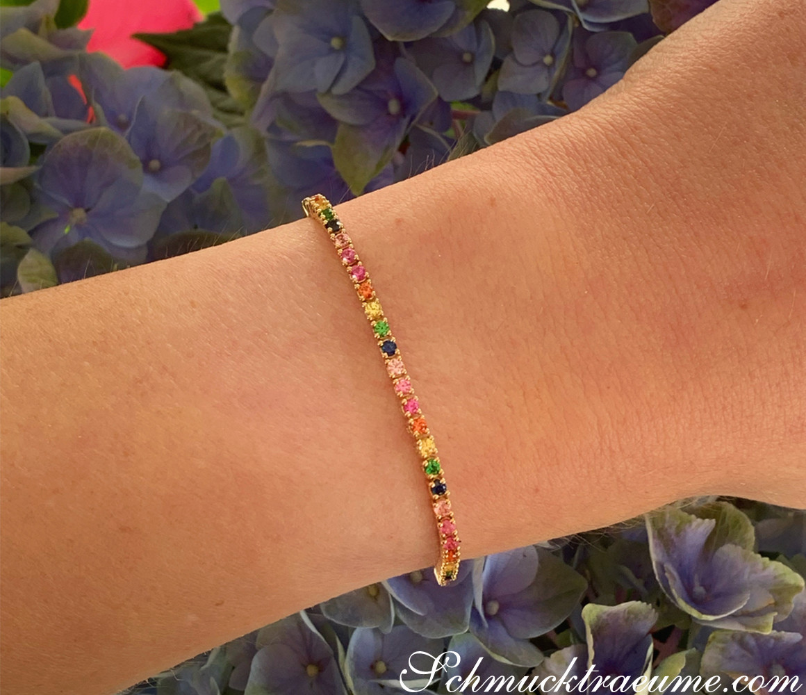 Goldenes Tennisarmband mit farbenfrohen Saphiren, Hintergrund mit Hortensienblüten.