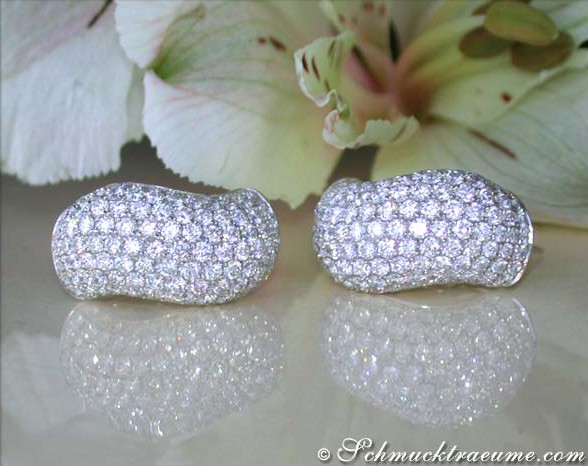 Diamantohrringe aus Weißgold, geschwungene Form, glänzende Brillanten, auf weißem Hintergrund mit Blume