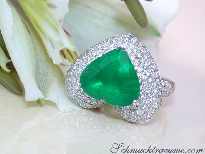 Weißgold-Smaragd-Herz-Ring mit Brillanten auf Blumenhintergrund