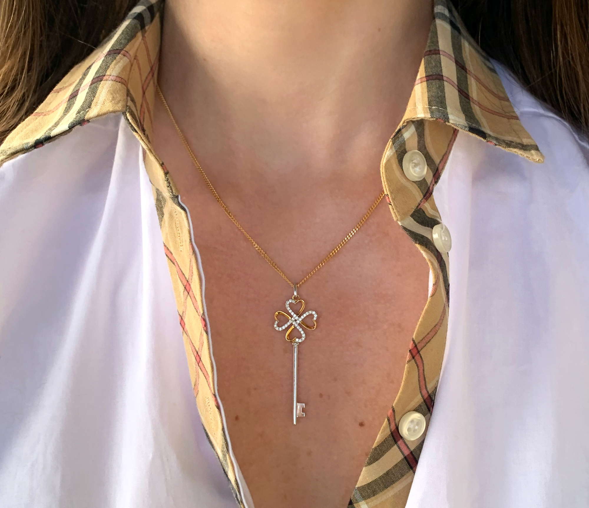 Goldene Schlüsselanhänger mit Brillanten auf kariertem Hemd, Detailaufnahme.