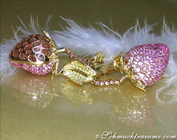 Goldene Erdbeer-Ohrgehänge mit pinken Saphiren, detailreich verziert, auf Federhintergrund.