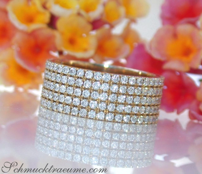 Flacher Diamantenring in Gelbgold 750, voller Brillanten, vor Blumenhintergrund Flacher Diamantenring in Gelbgold 750, voller Brillanten, vor Blumenhintergrund