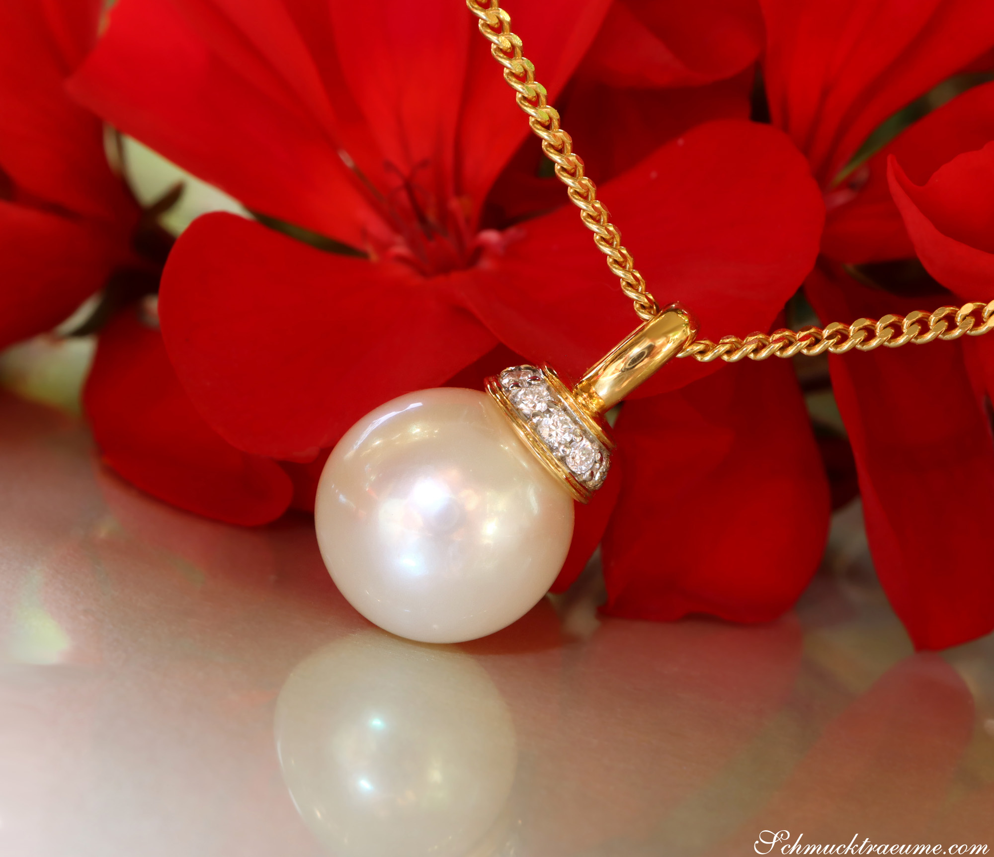 Goldkette mit Perlenanhänger und Diamanten, vor roten Blüten.