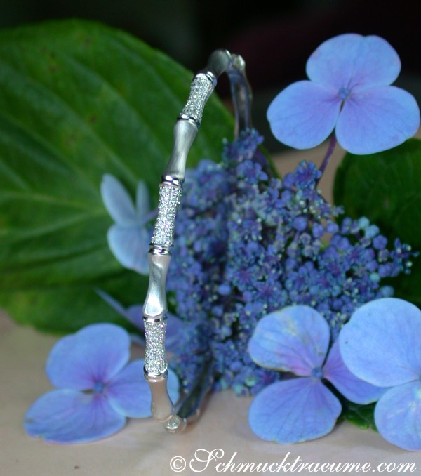 Silberner Diamantarmreif im Bambus-Stil auf Blütenhintergrund