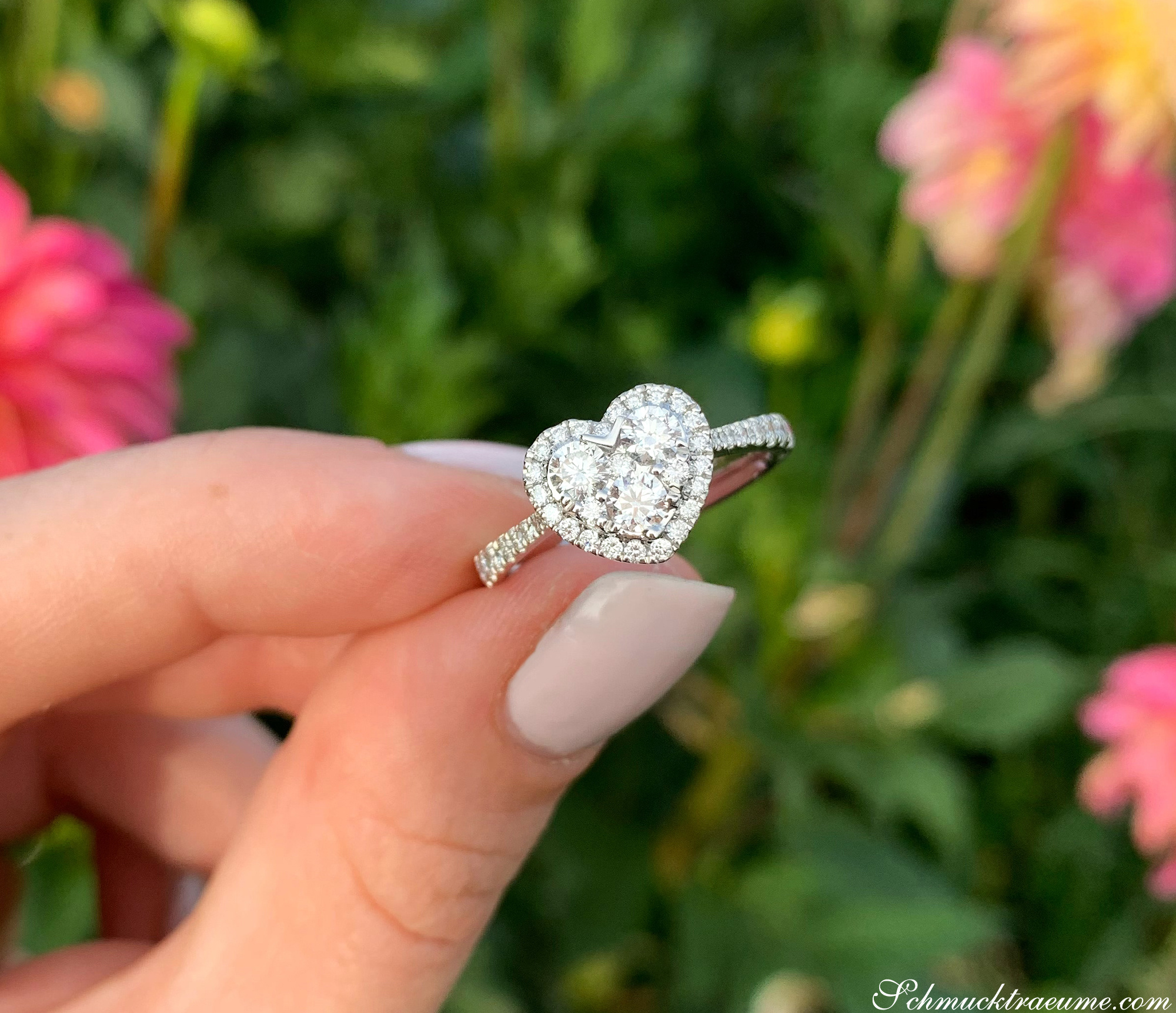 Herzring aus Weißgold 750, funkelndes VS-Brillantenherz, Detailaufnahme, im Hintergrund Blüten.