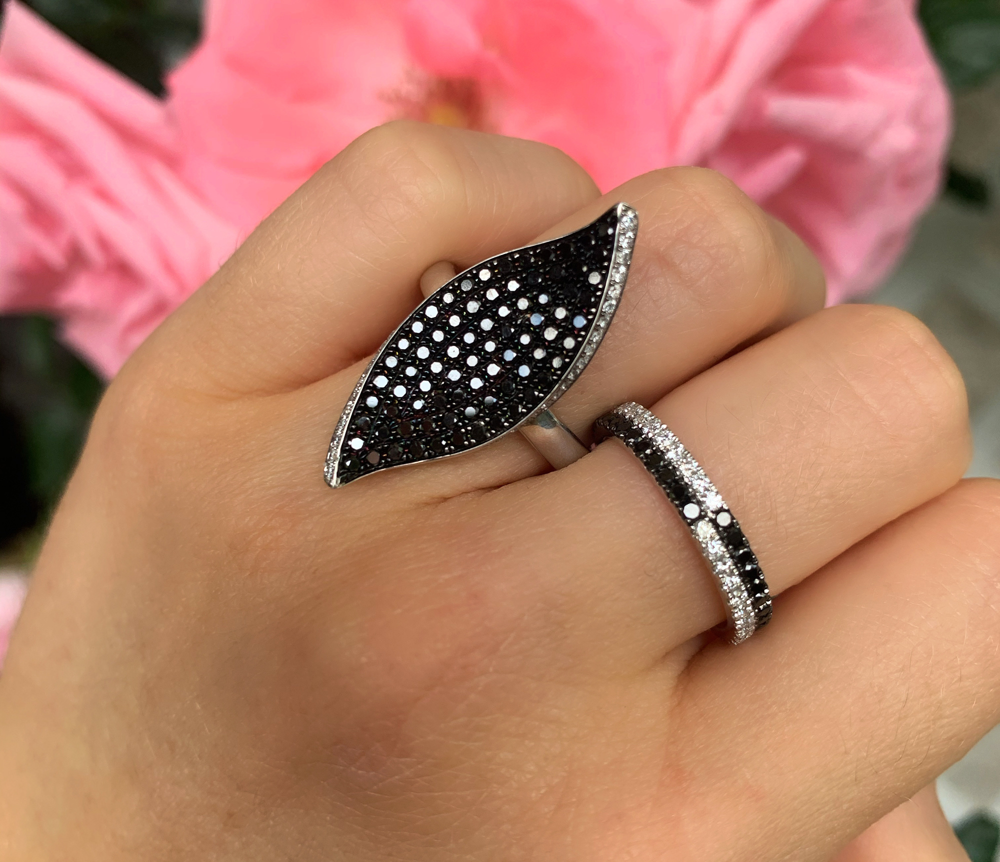 Schwarz-Weiß-Diamanten-Ring im Blatt-Design, Detailaufnahme, auf Hand getragen, vor rosa Blume.