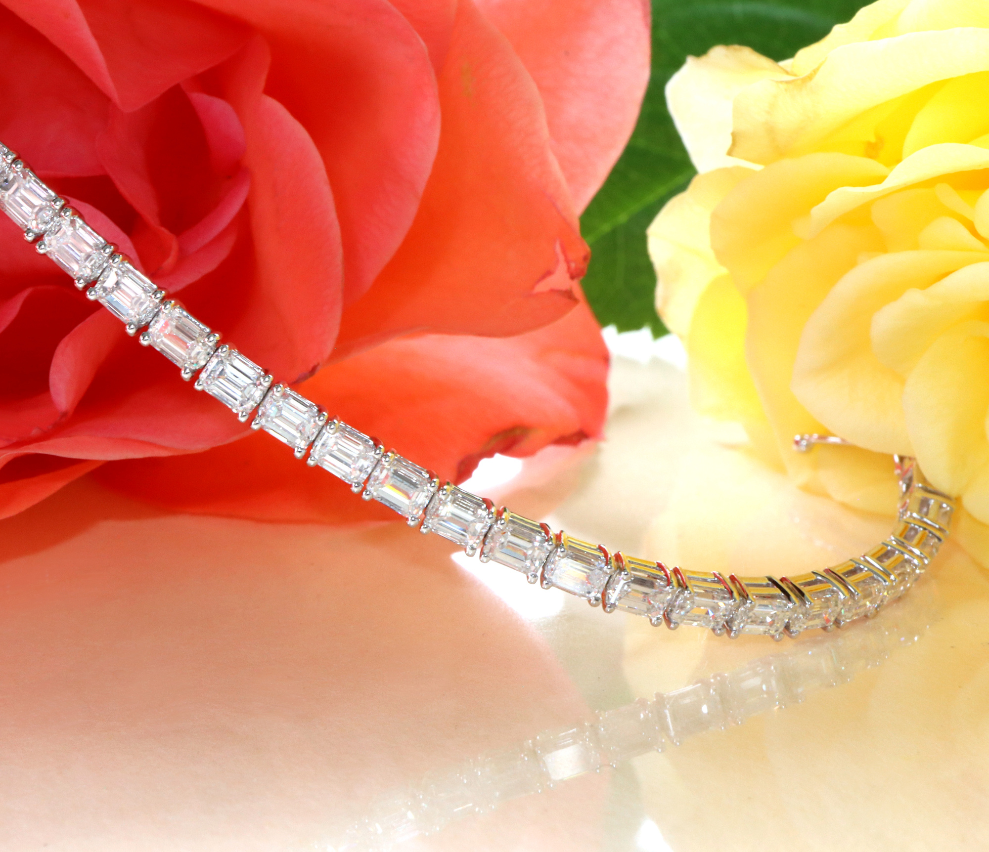 Diamant-Tennisarmband mit Smaragdschliff-Diamanten, Rosenblüten im Hintergrund.
