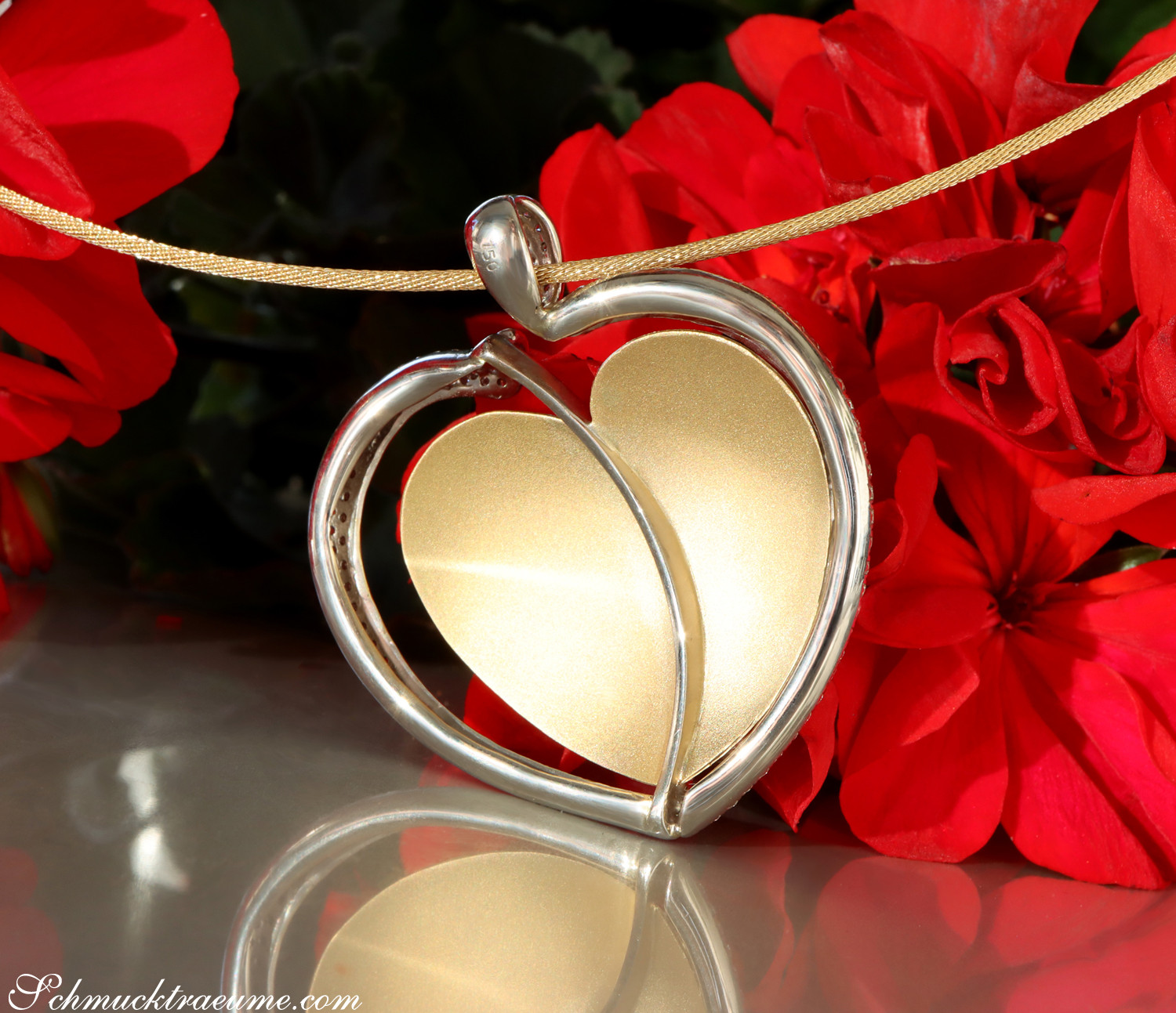 Herz-Anhänger aus Gelbgold mit Brillanten, goldenes Band, rote Blüten im Hintergrund