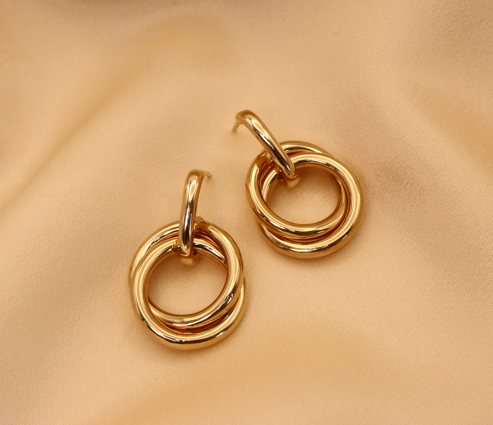 Goldene Ohrringe mit verschränkten Ringen auf cremefarbenem Stoff