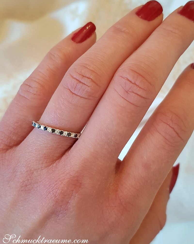 Schwarze und weiße Diamanten in Weißgold auf zartem Finger, Nagellack rot.