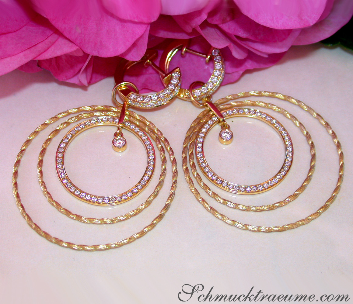 Kreisförmige Ohrringe aus gelbgemachtem Gold mit Brillanten, vor Rosenblüten.