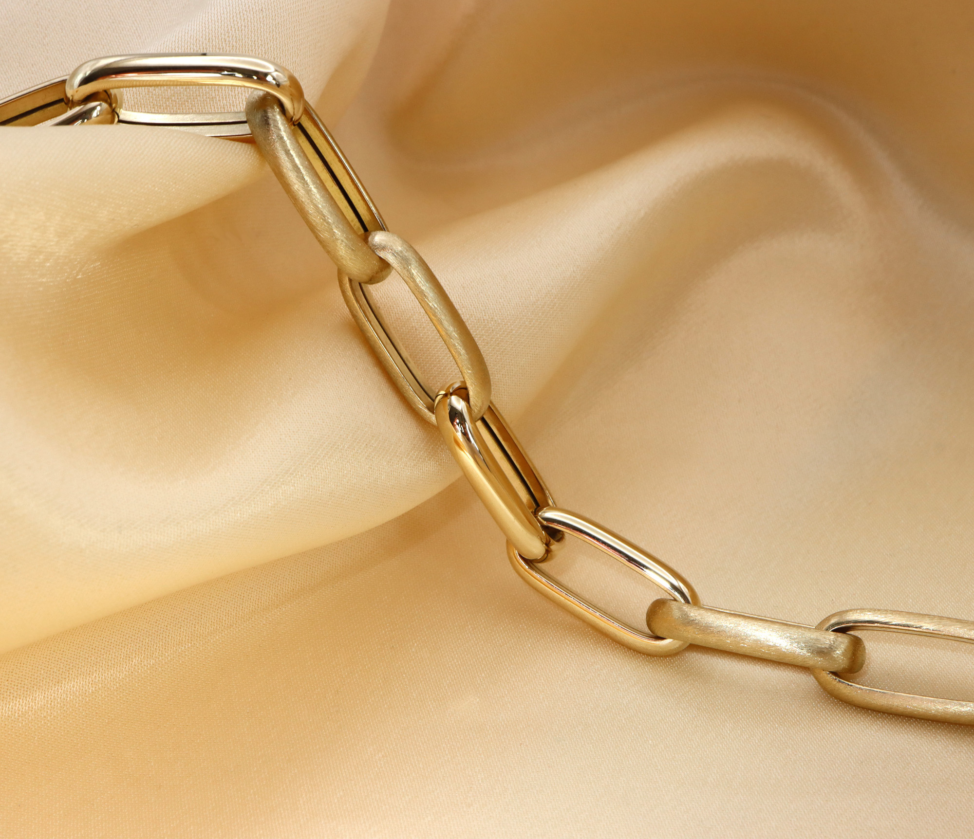 Goldenes Paperclip-Armband auf satiniertem Stoff, Detailaufnahme der Verbindungskette.