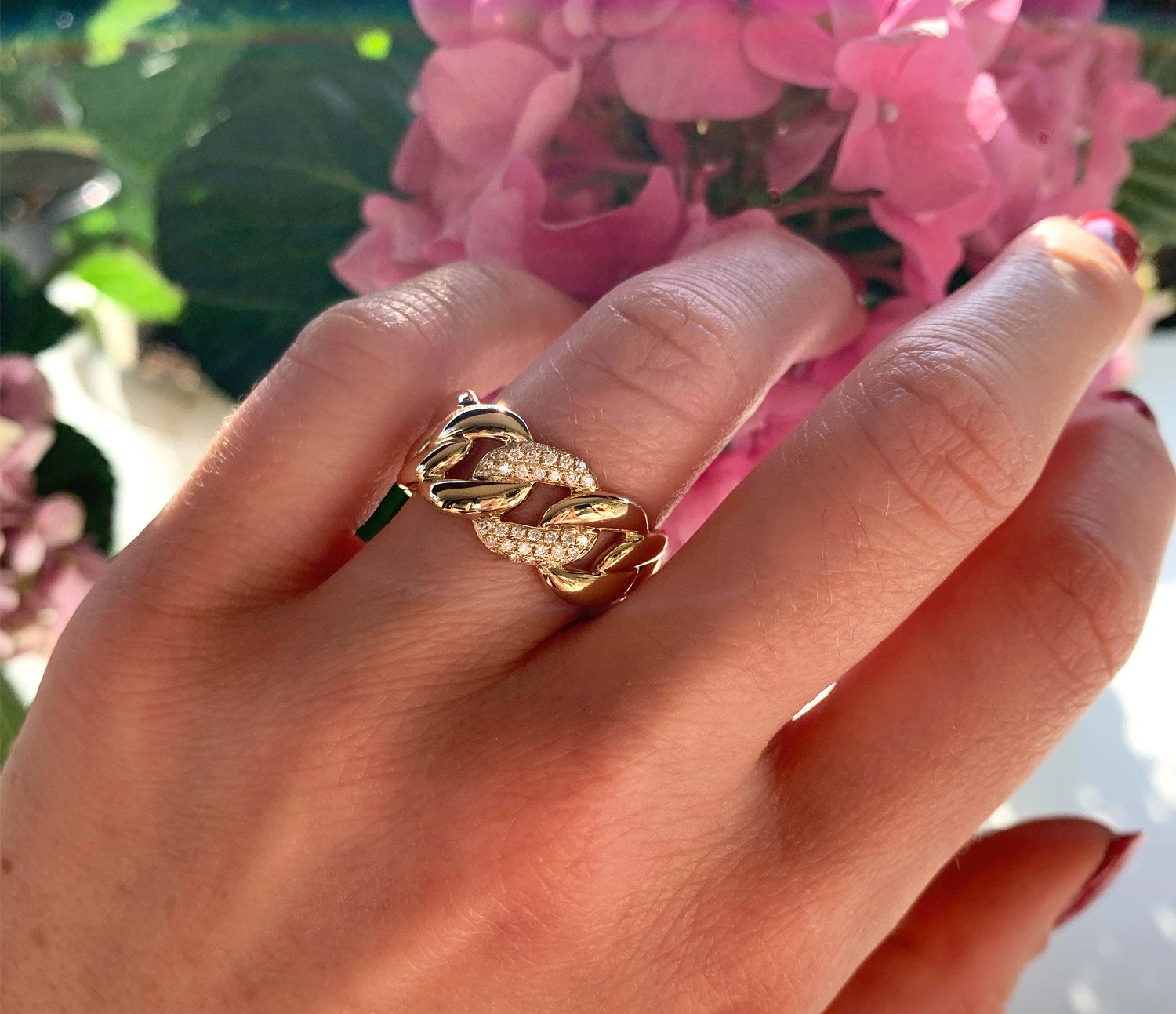 Goldener Panzerkettenring mit Brillanten auf blühendem Hintergrund