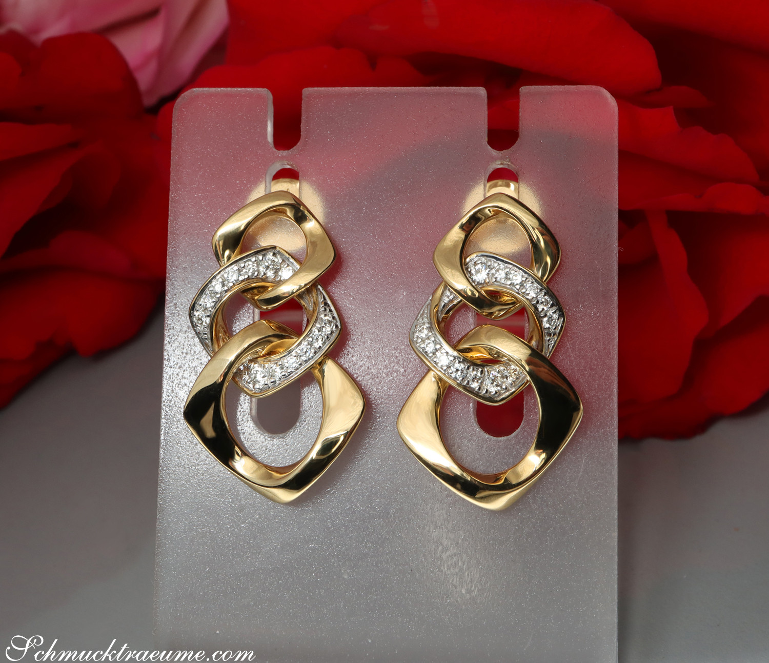 Goldene Glieder-Ohrringe mit Brillanten auf Display vor Rosenblättern