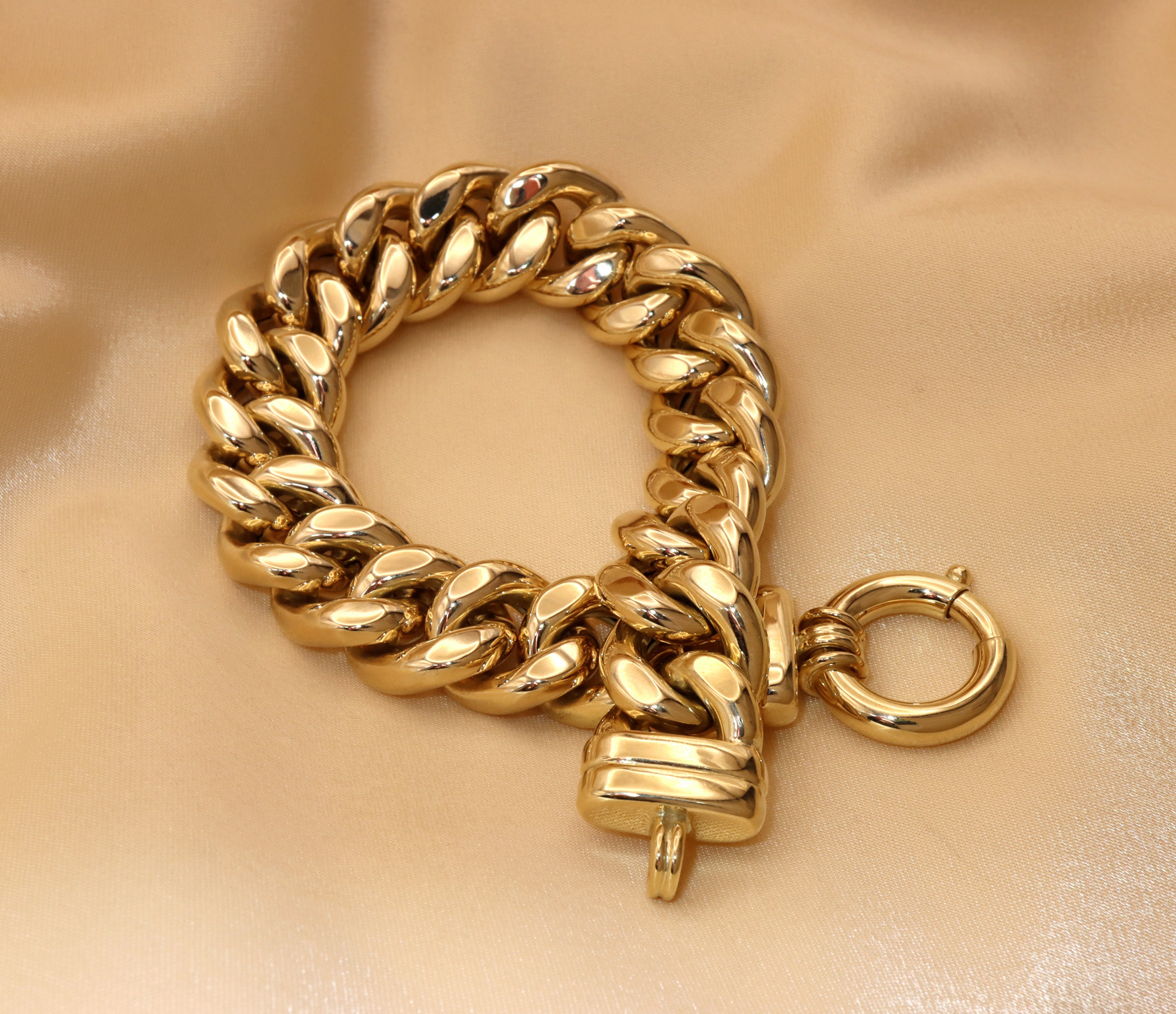 Goldene Panzerarmband auf cremefarbener Seide, Detailaufnahme, glänzend, geschwungenes Design