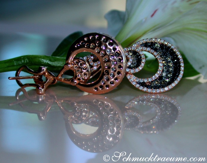 Schwarze Diamanten-Ohrstecker mit Roségold und Glitzerdetails, auf Blütenblatt abgebildet.