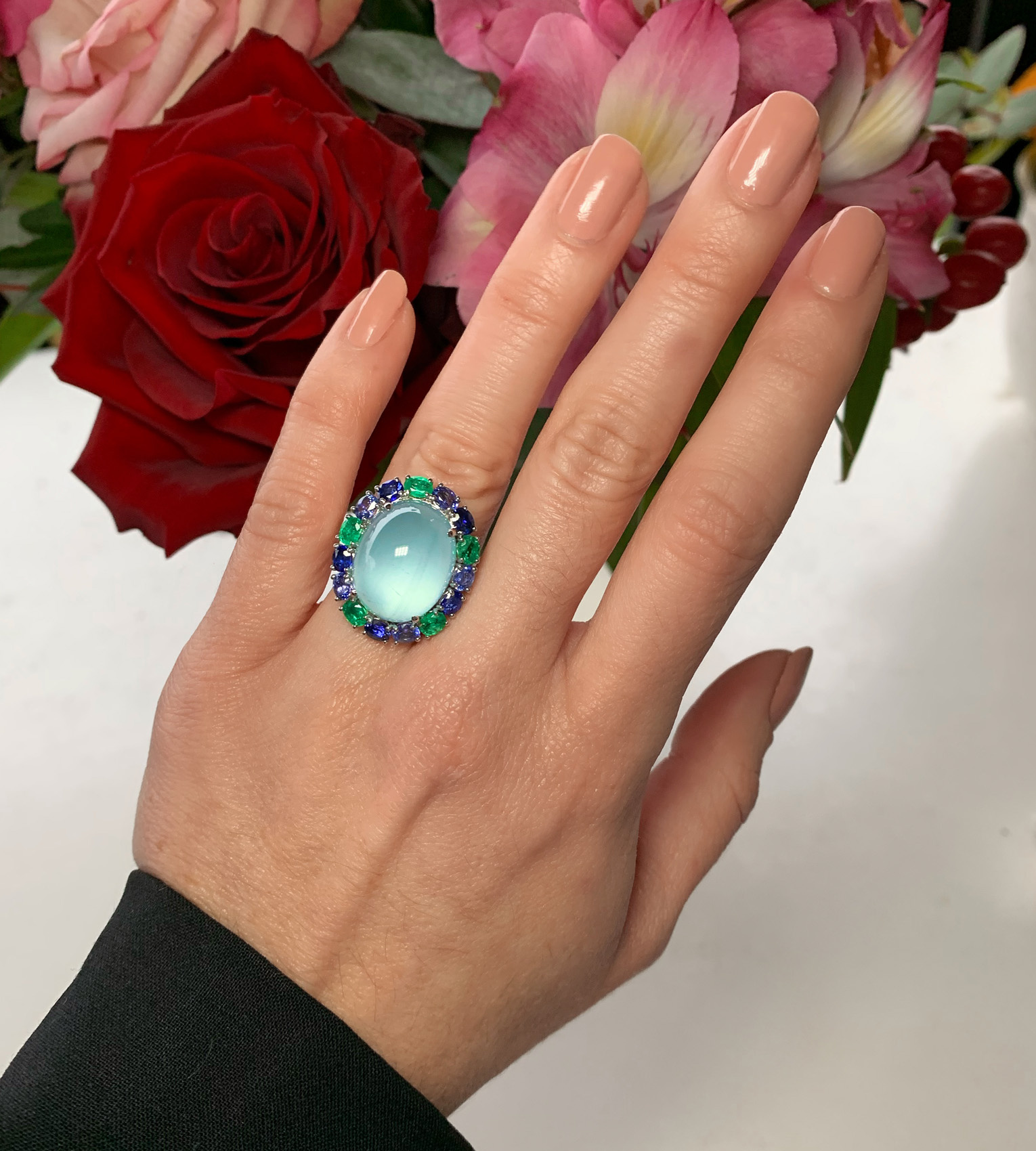 Milky Aquamarin-Ring mit Saphiren und Smaragden auf Hand vor Rosenblüten